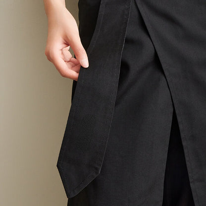 Close-up of a person wearing a black work apron with a neutral background