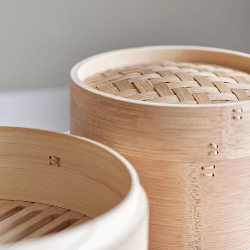 Close-up of a bamboo steamer with woven lid on a white surface.