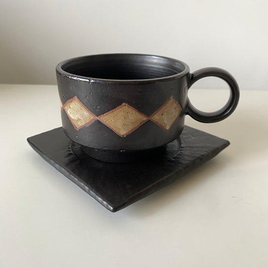 Black ceramic cup with geometric design on a matching saucer against a white background