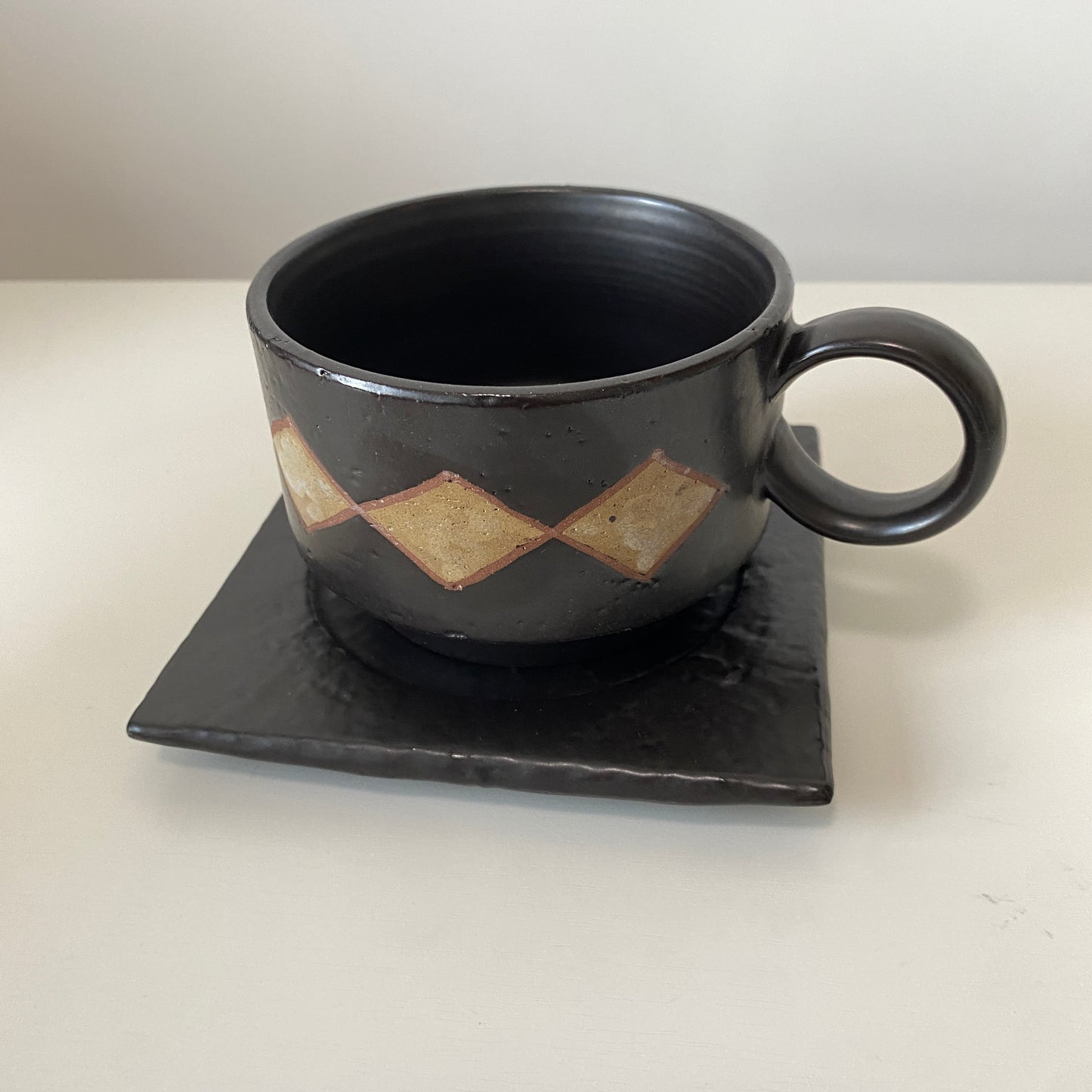 Black ceramic cup with geometric design on a matching coaster against a white background