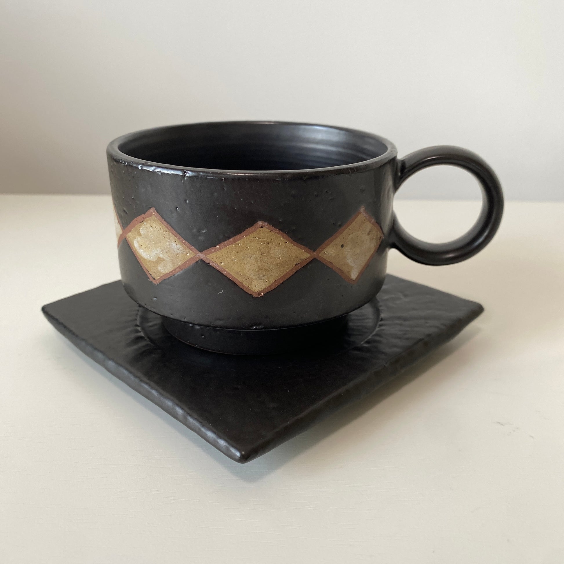 Black ceramic cup with geometric patterns on a matching saucer against a white background