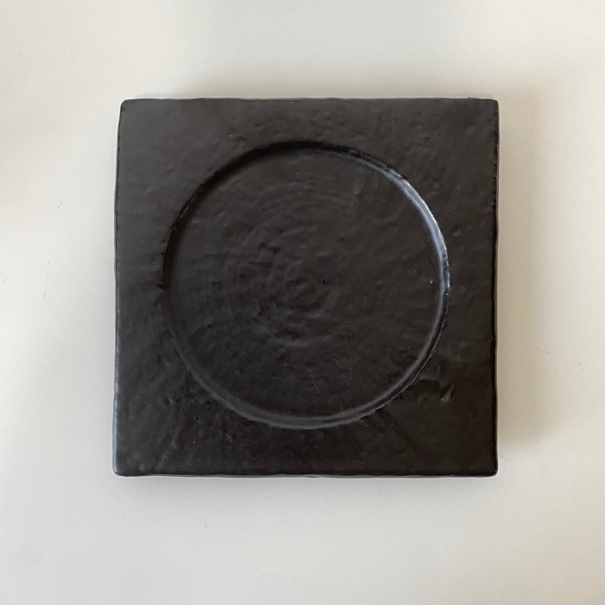 Black square coaster with circular depression on a white background