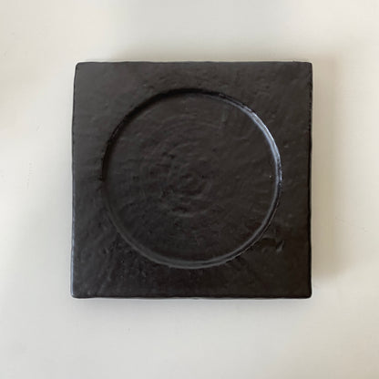 Black square coaster with circular depression on a white background